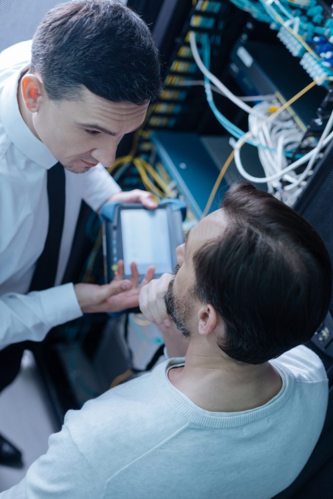 Two men are looking at a computer in a server room.