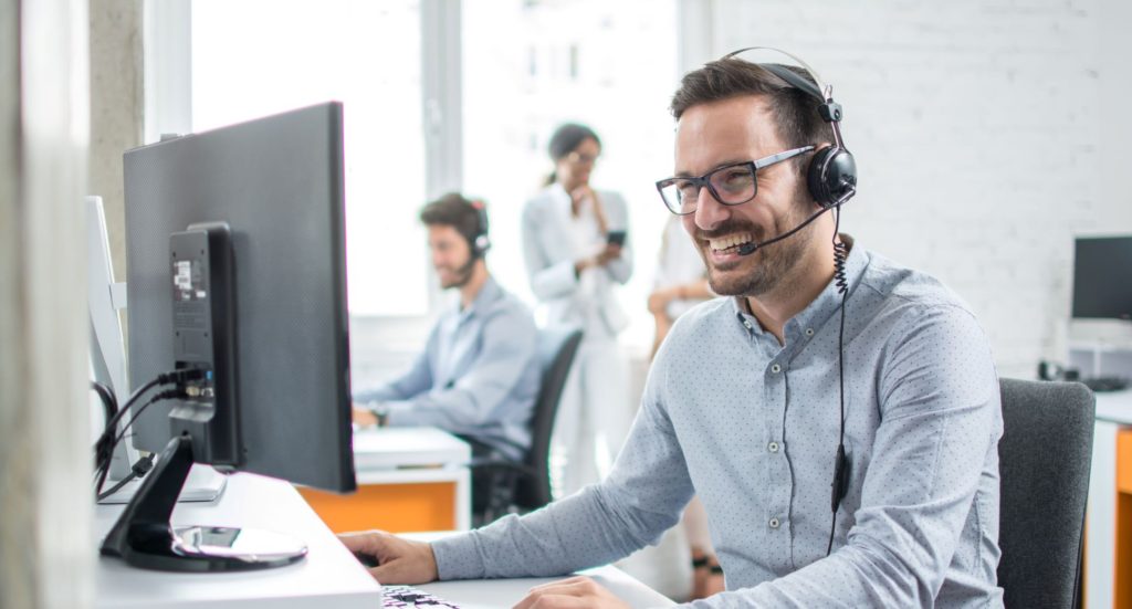 A man in a call center wearing a headset can be seen at work.